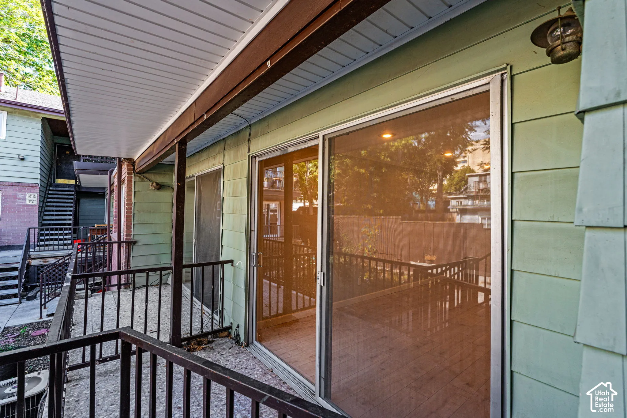 Outdoor patio with black metal railings, sliding glass door entry, and green shingle siding