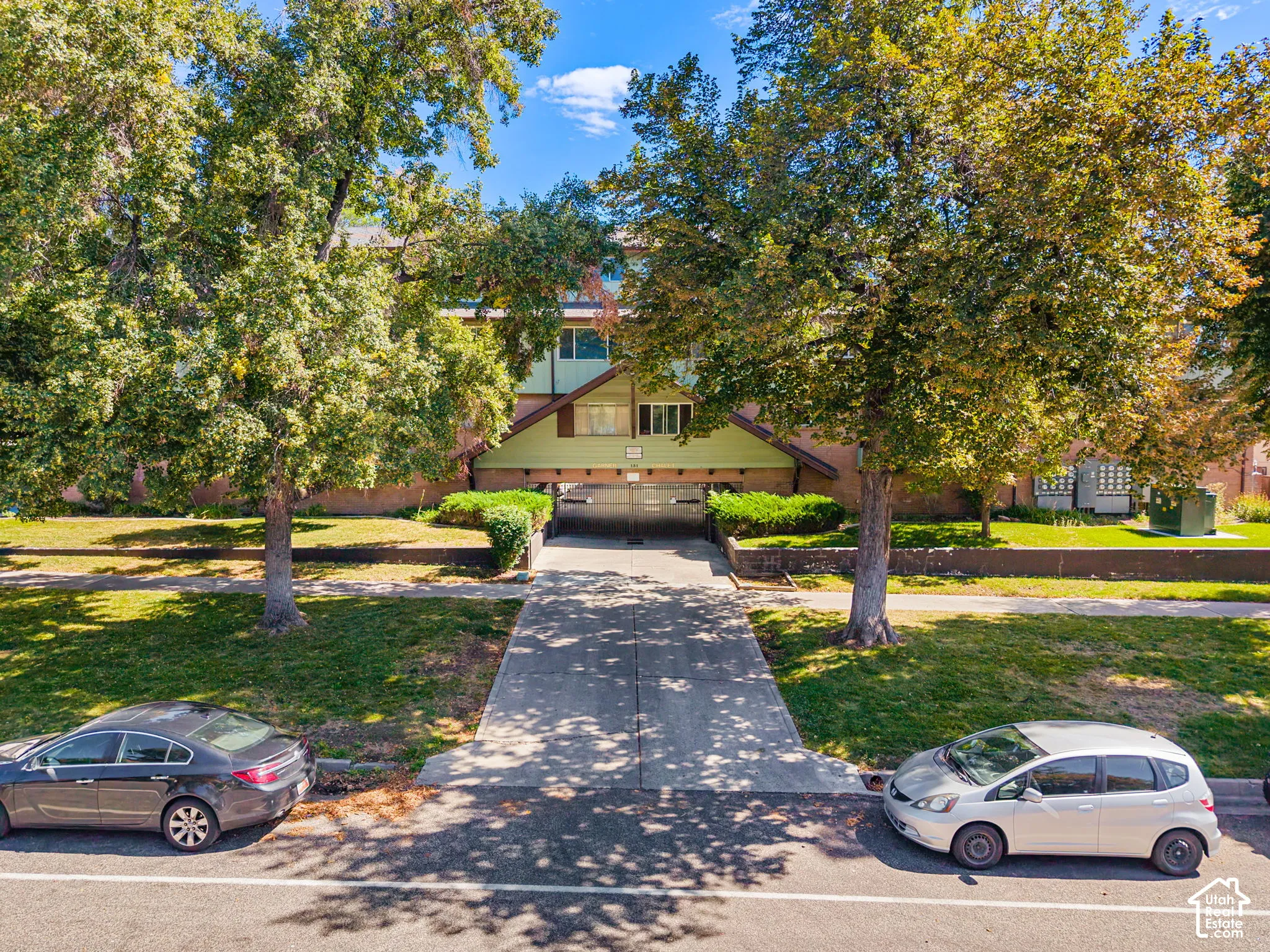 Multi-story building exterior with mature trees, green lawn areas, and a concrete pathway
