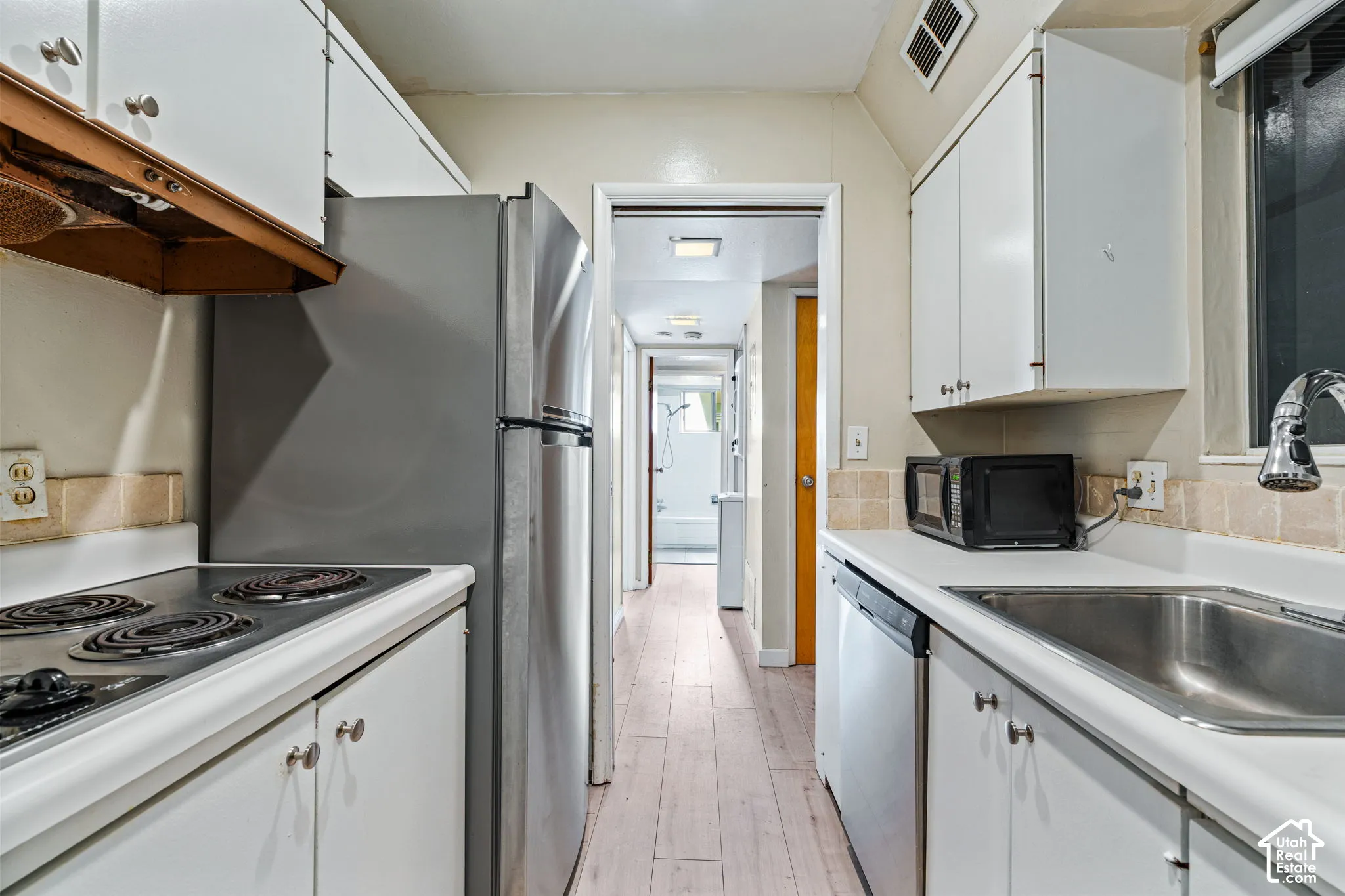 Galley kitchen with white cabinetry, stainless steel refrigerator, electric range, and single-basin sink