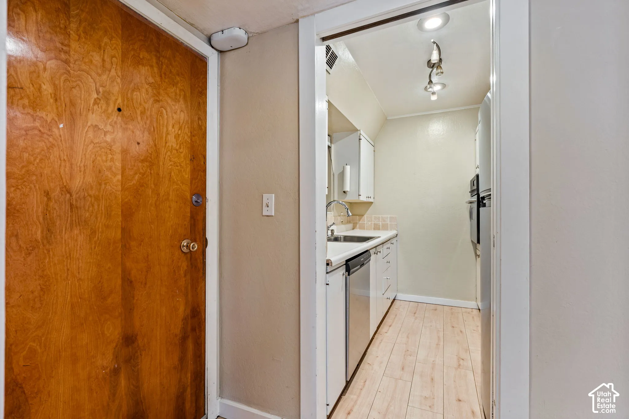 Compact kitchen featuring wood-finish flooring, white cabinetry, integrated stainless steel dishwasher, and wall-mounted oven