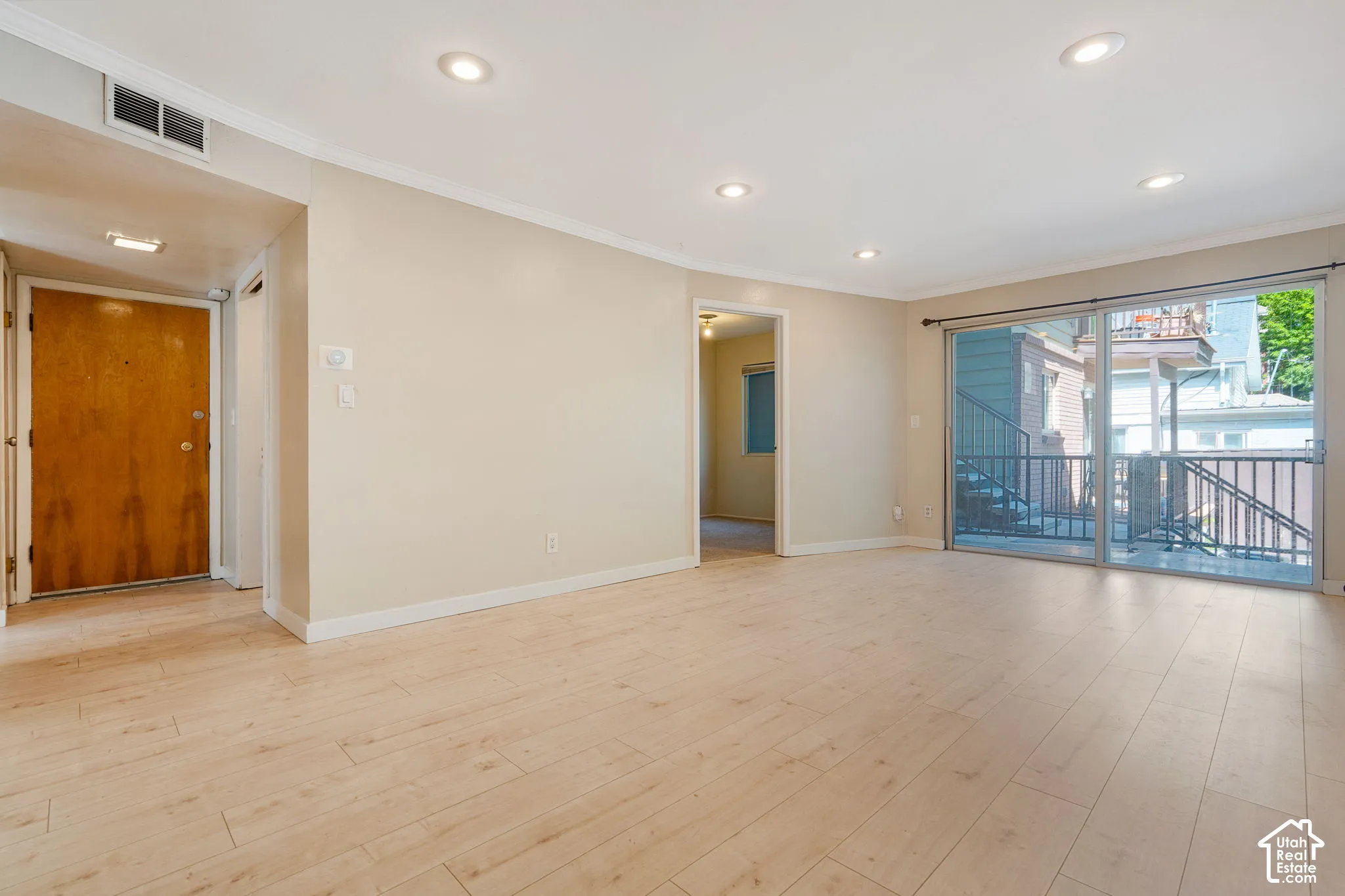 Light wood-finish flooring complemented by recessed ceiling lighting and crown molding