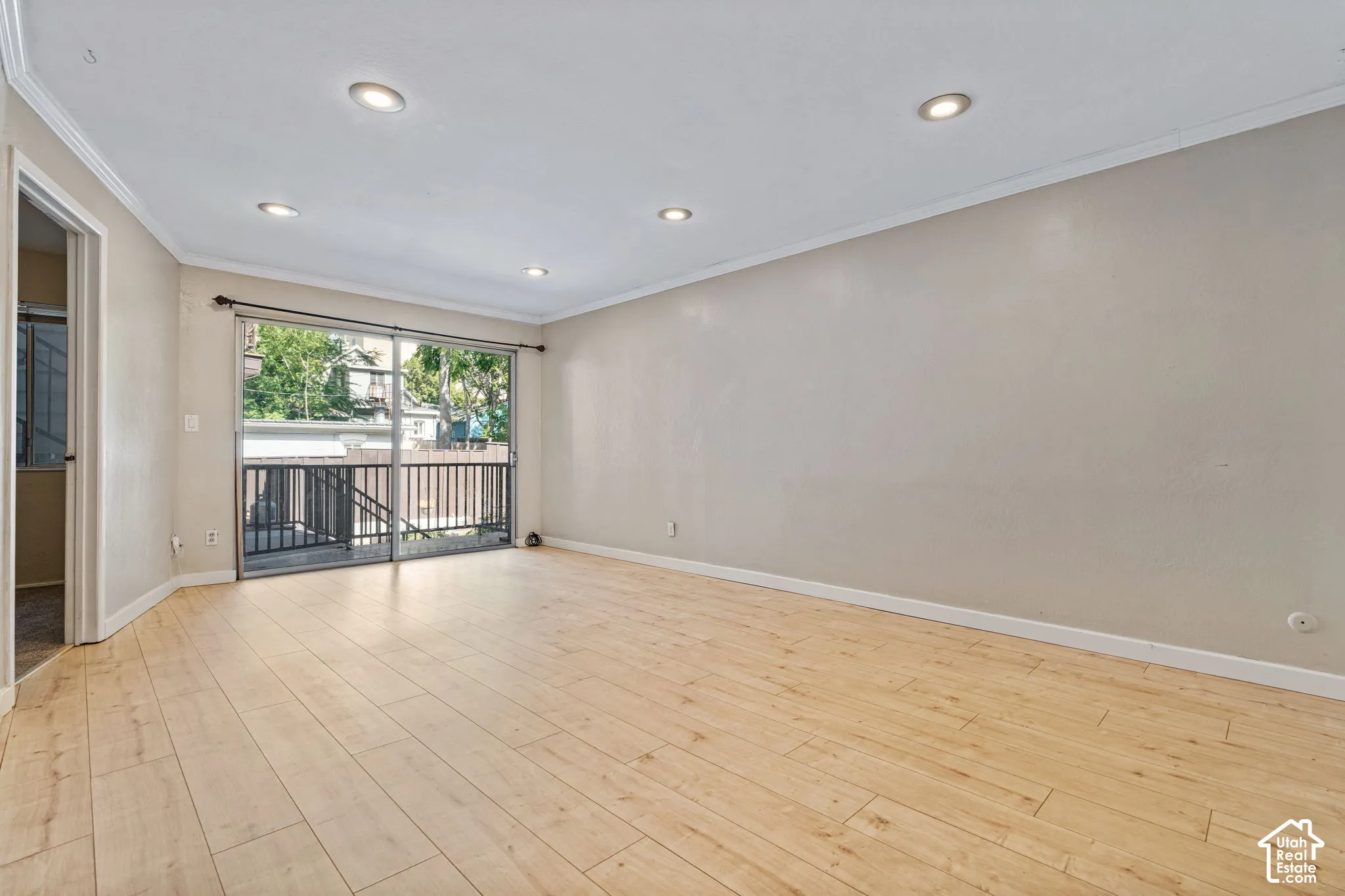 Recessed ceiling lighting, crown molding, wood-finish flooring, and sliding glass doors to a private balcony with black metal railings