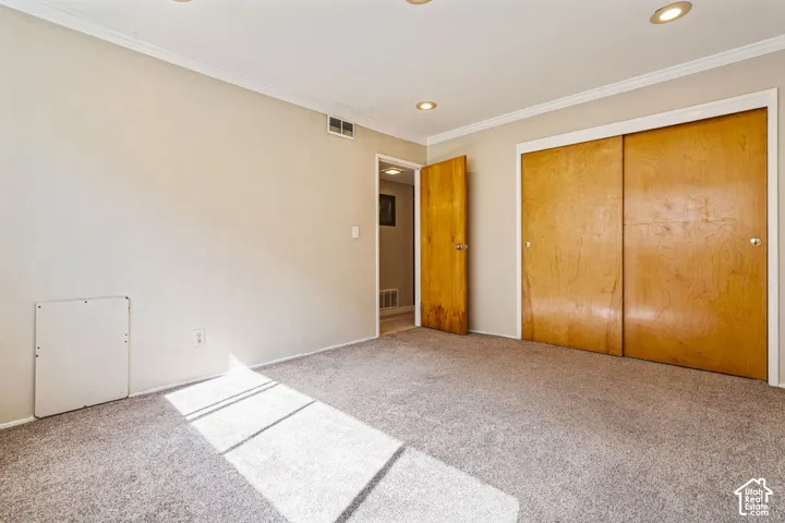 Neutral-toned carpeting with light walls, featuring recessed lighting, crown molding, and wood-finish closet doors
