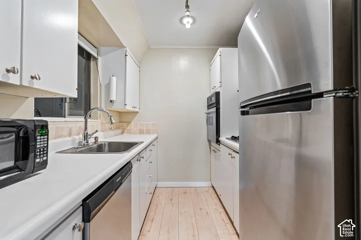 Galley kitchen featuring white cabinetry, light countertops, stainless steel refrigerator, stainless steel dishwasher, and a built-in wall oven