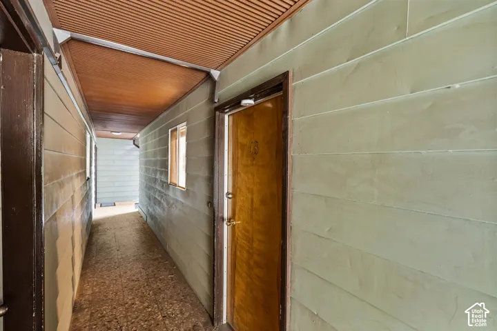 Corridor with textured ceiling panels, wood-finish door, and horizontal siding