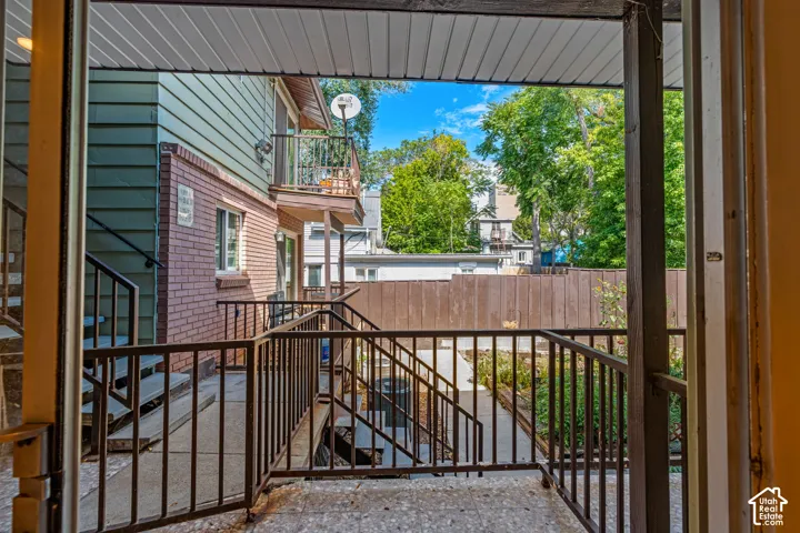 Exterior patio with metal railings and concrete flooring, featuring a brick and siding facade, and a private balcony