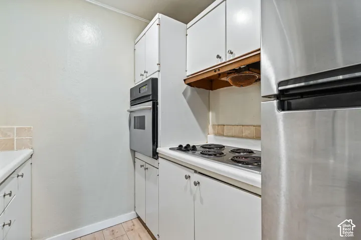 White cabinetry, stainless steel refrigerator, built-in oven, electric stovetop, tile backsplash