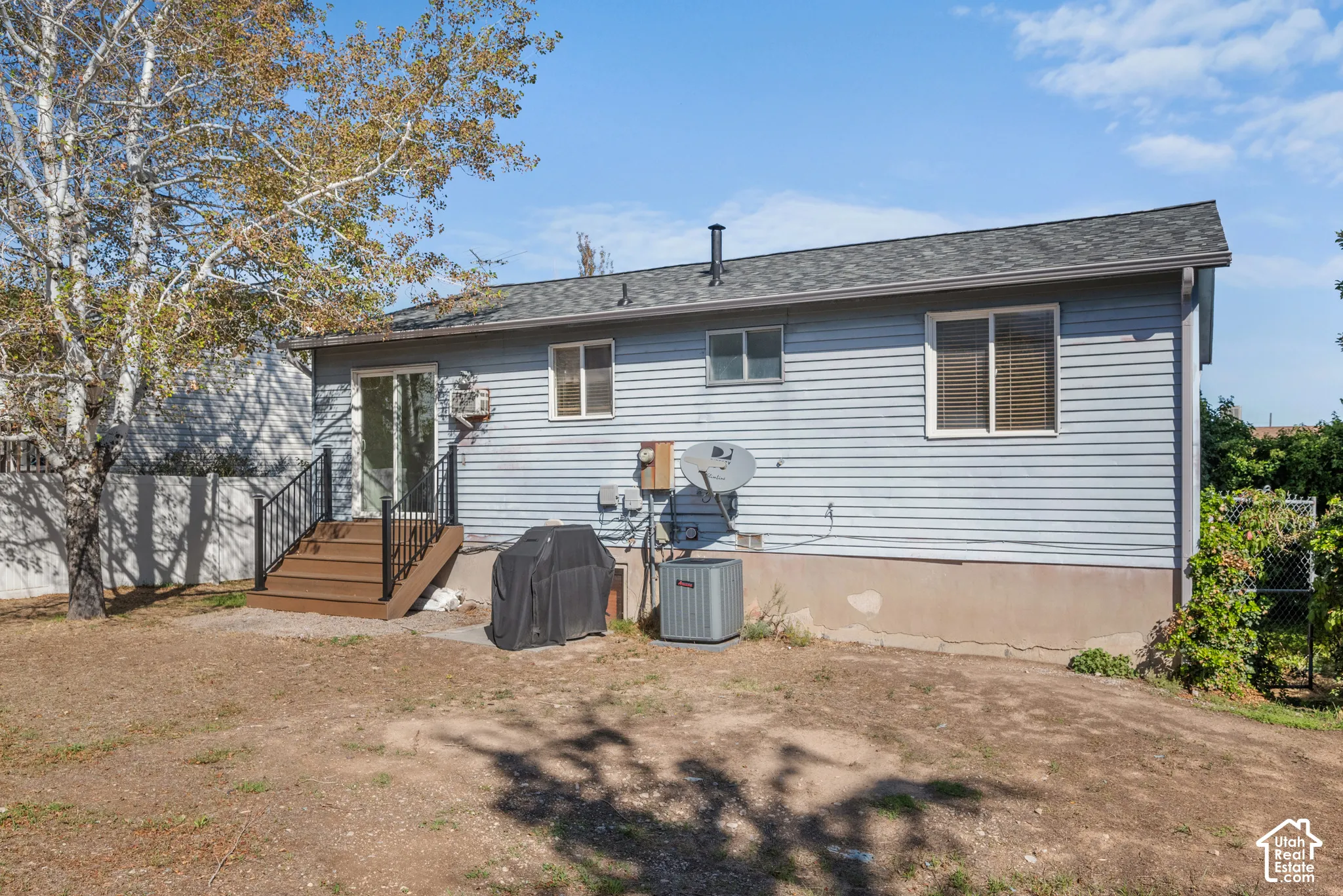 Rear exterior featuring light blue horizontal siding, a gabled roof, and a wood-tone deck with black railings