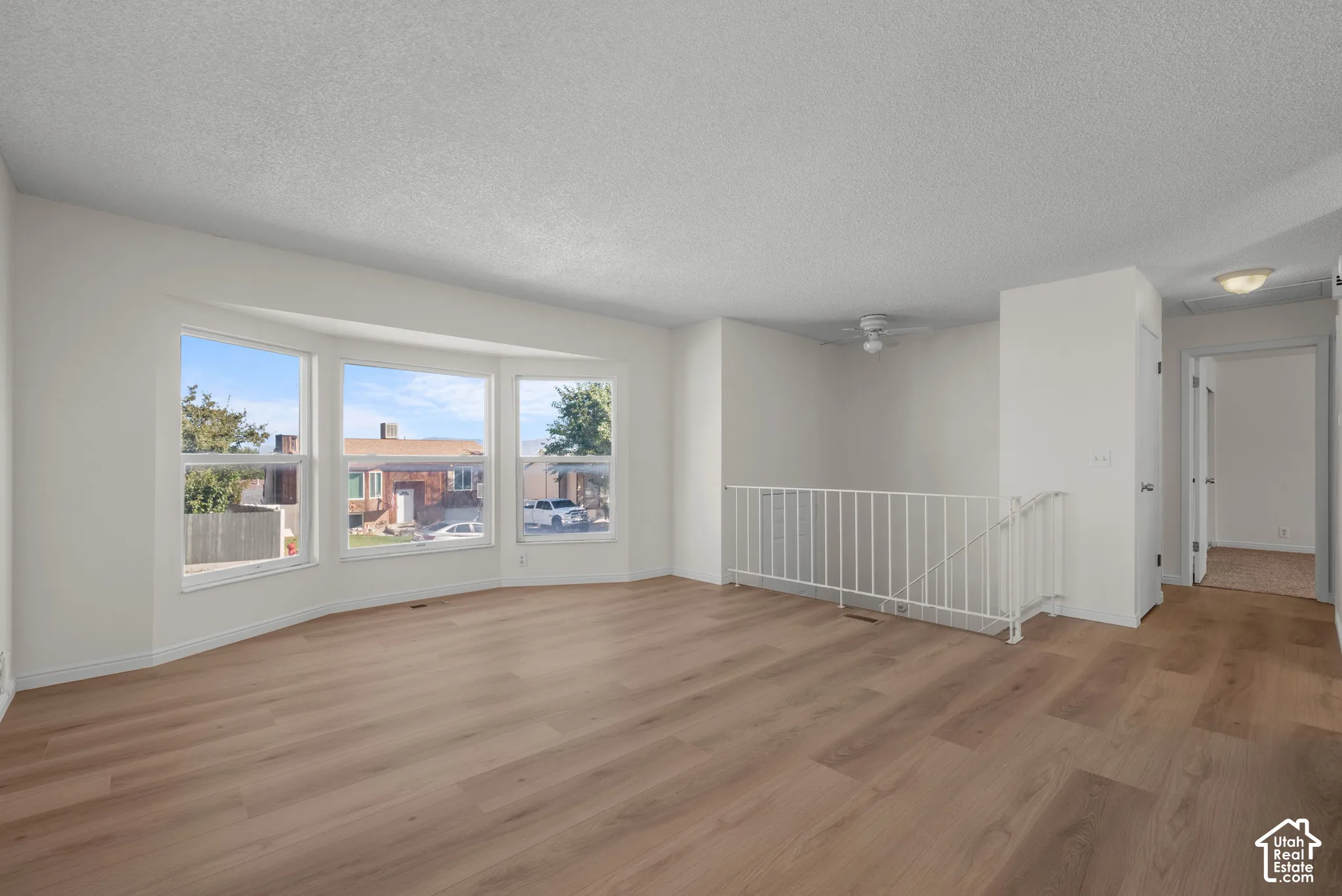Spacious interior featuring wood-finish flooring, white walls, multiple windows, and a white railing