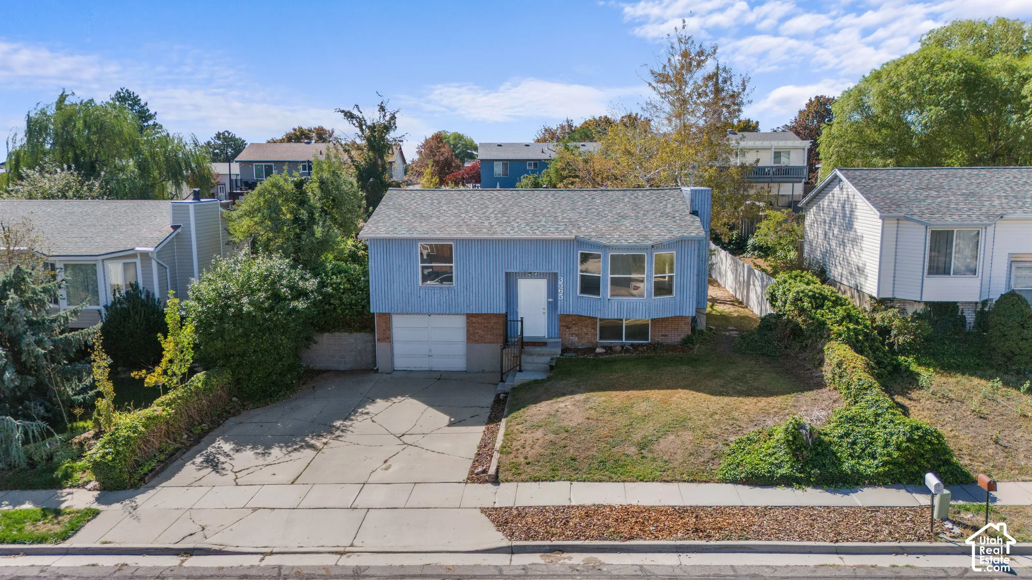 Blue exterior with white trim, attached garage, concrete driveway, and mature landscaping
