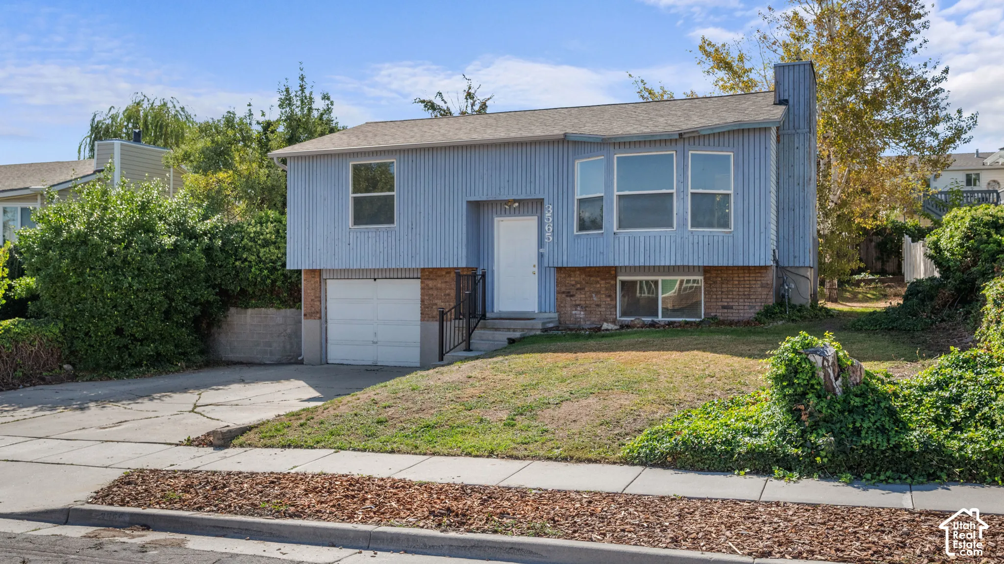 Split-level residence featuring a single-car garage, brick foundation, and light blue siding