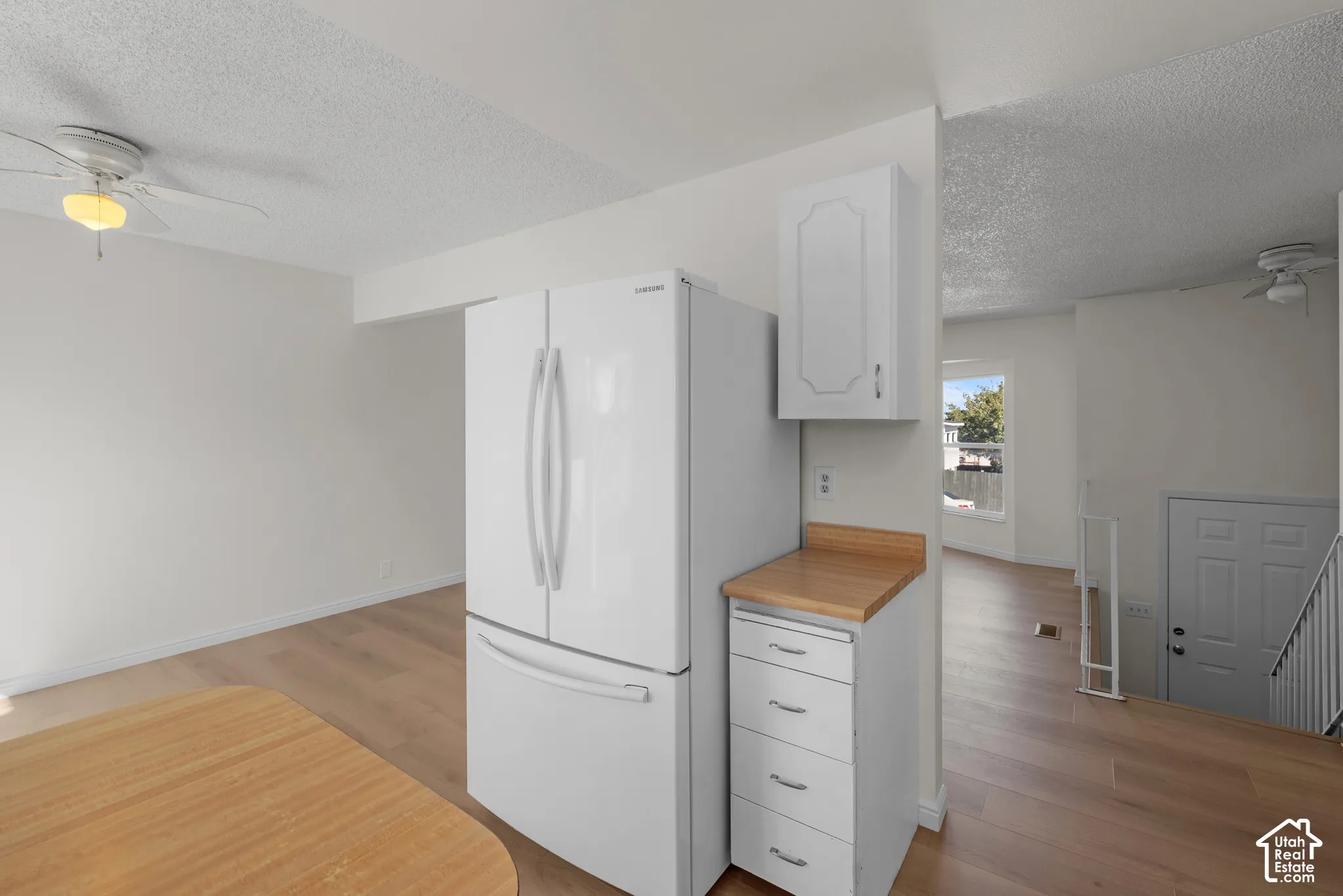 Wood-finish flooring throughout, white cabinetry with wood-finish countertop, white refrigerator, and ceiling fan with integrated lighting
