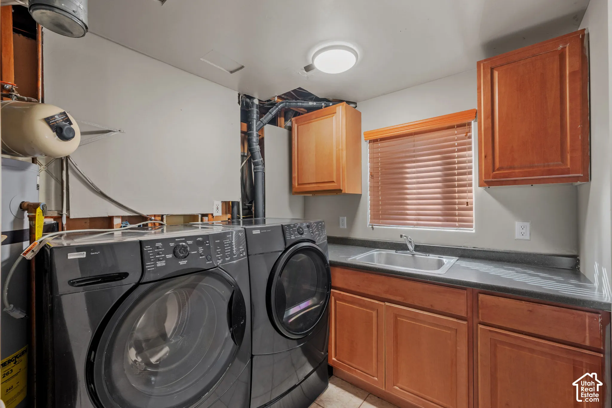 Functional utility area featuring a built-in sink, wood-finish cabinetry, countertop space, and window with blinds