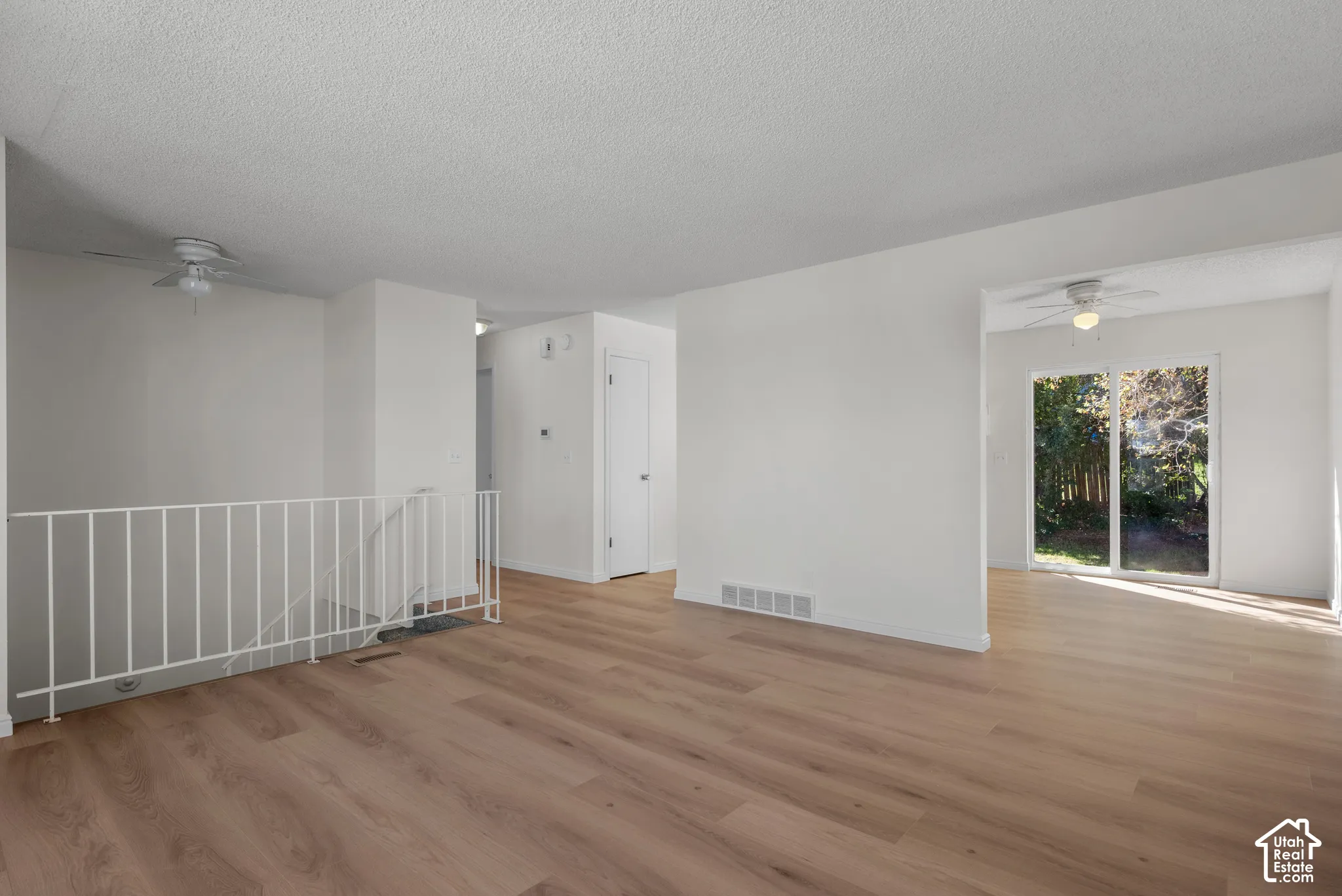 Expansive room with wood-finish flooring, white walls, and a ceiling fan