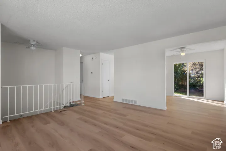 Expansive room with wood-finish flooring, white walls, and a ceiling fan