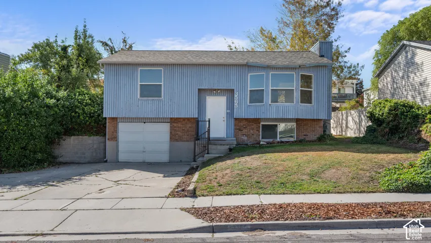 Split-level residence featuring vertical siding, brick accents, a front-facing garage, and a concrete driveway