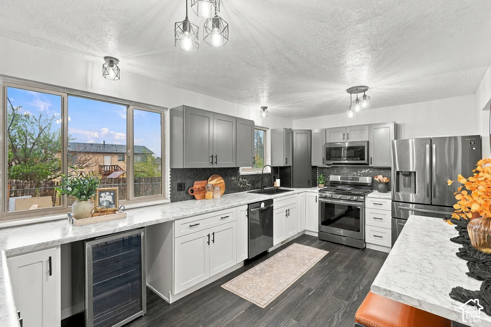Kitchen featuring soft-close updated two-tone cabinetry, high-end stainless steel appliances, dark tile backsplash, and light countertops.