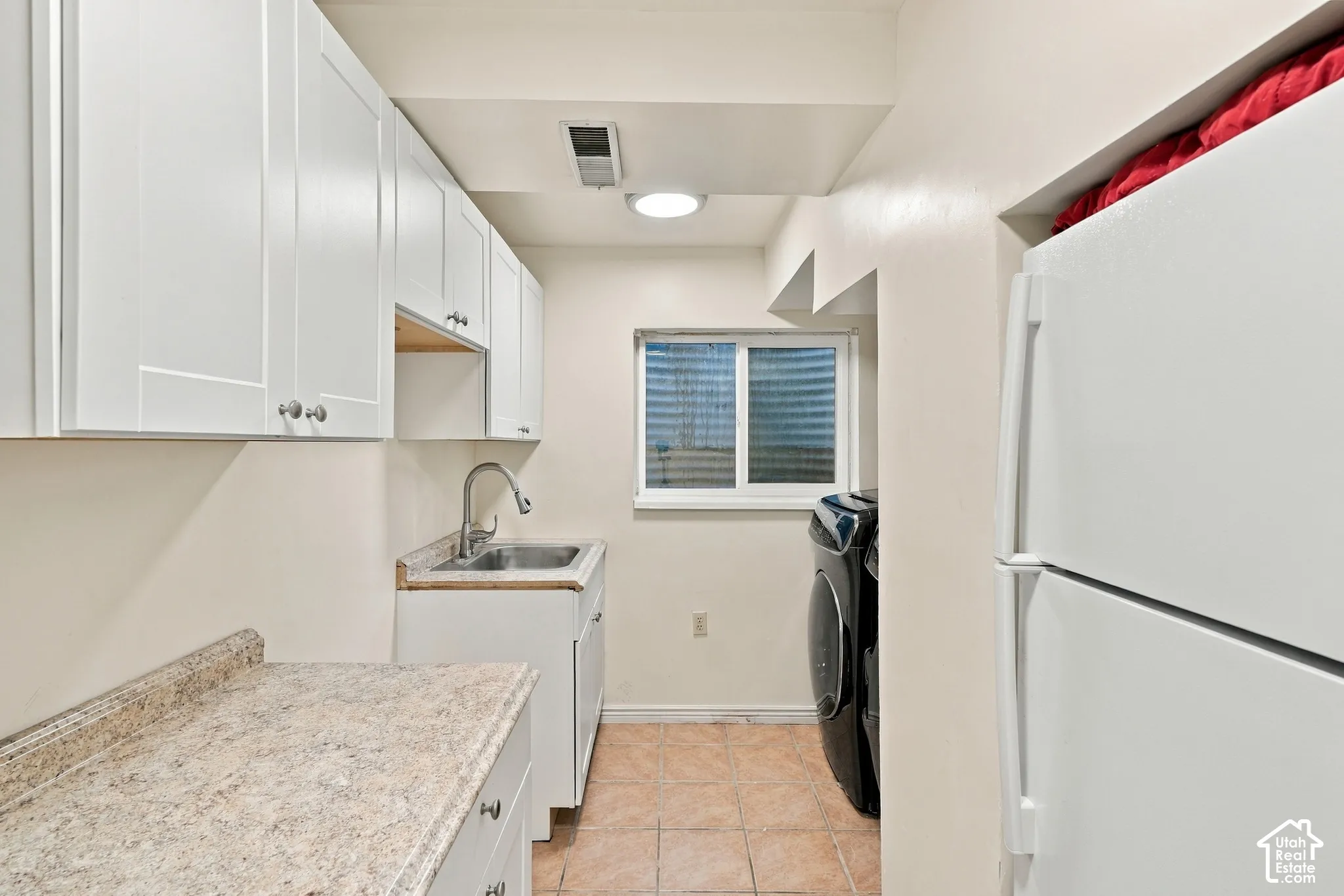 White shaker-style cabinetry with chrome hardware, speckled countertop, and stainless steel sink and high-end washer/dryer