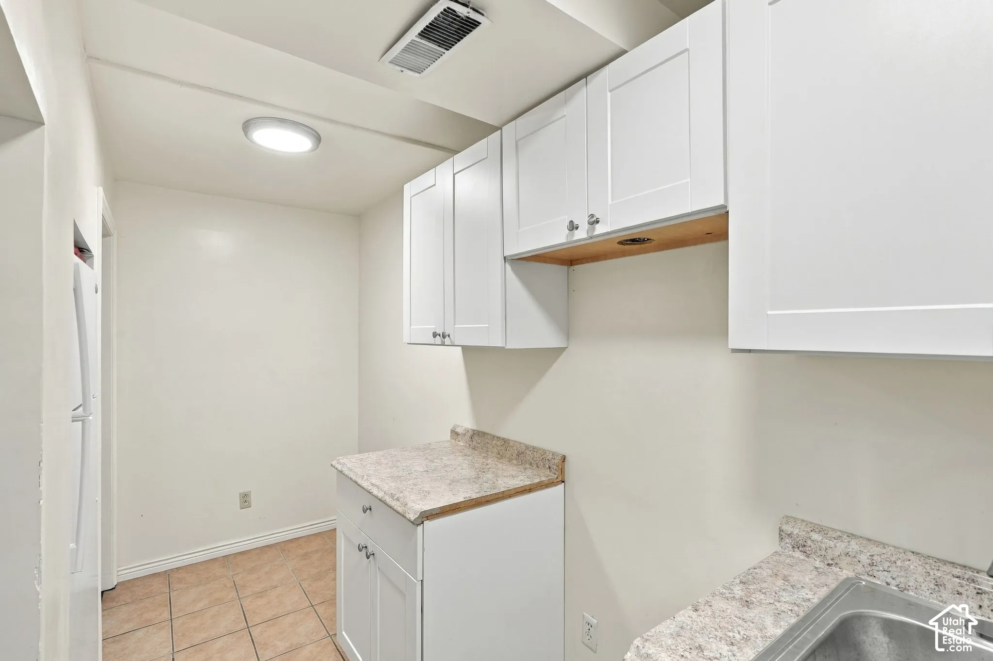 Basement 2nd Kitchen featuring white shaker-style cabinetry, light-colored countertops, tile flooring, stainless steel sink, and included fridge.