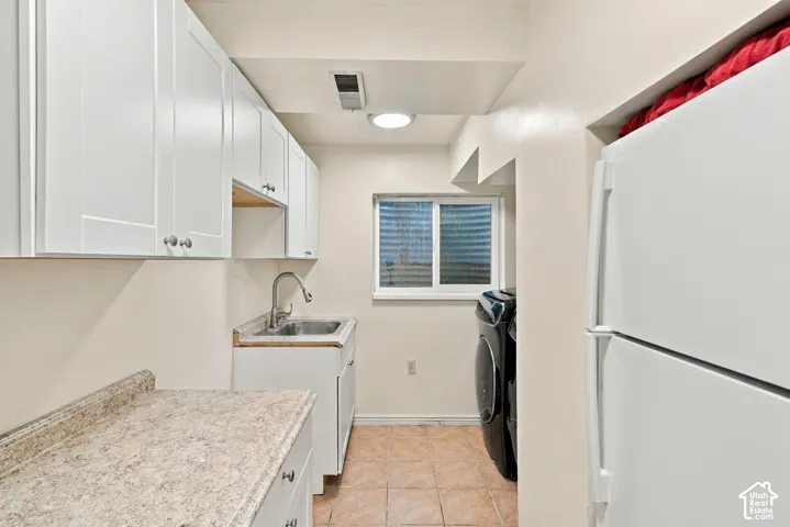 White shaker-style cabinetry with chrome hardware, speckled countertop, and stainless steel sink and high-end washer/dryer