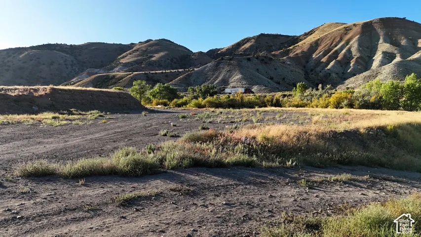 Expansive unpaved terrain with low-growing vegetation, backed by rolling hills and distant mountainous topography