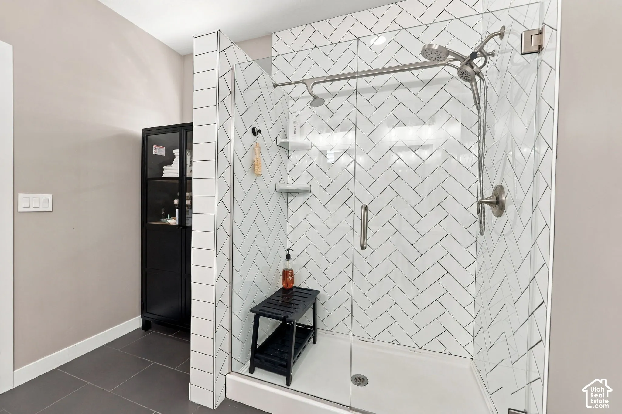 Glass-enclosed shower with white herringbone tile surround, dual shower heads, and brushed nickel fixtures