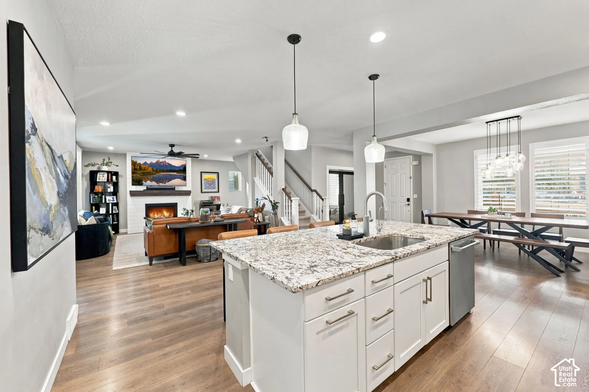 Open-concept layout featuring wood-finish flooring, a kitchen island with stone countertop, stainless steel sink, and pendant lighting