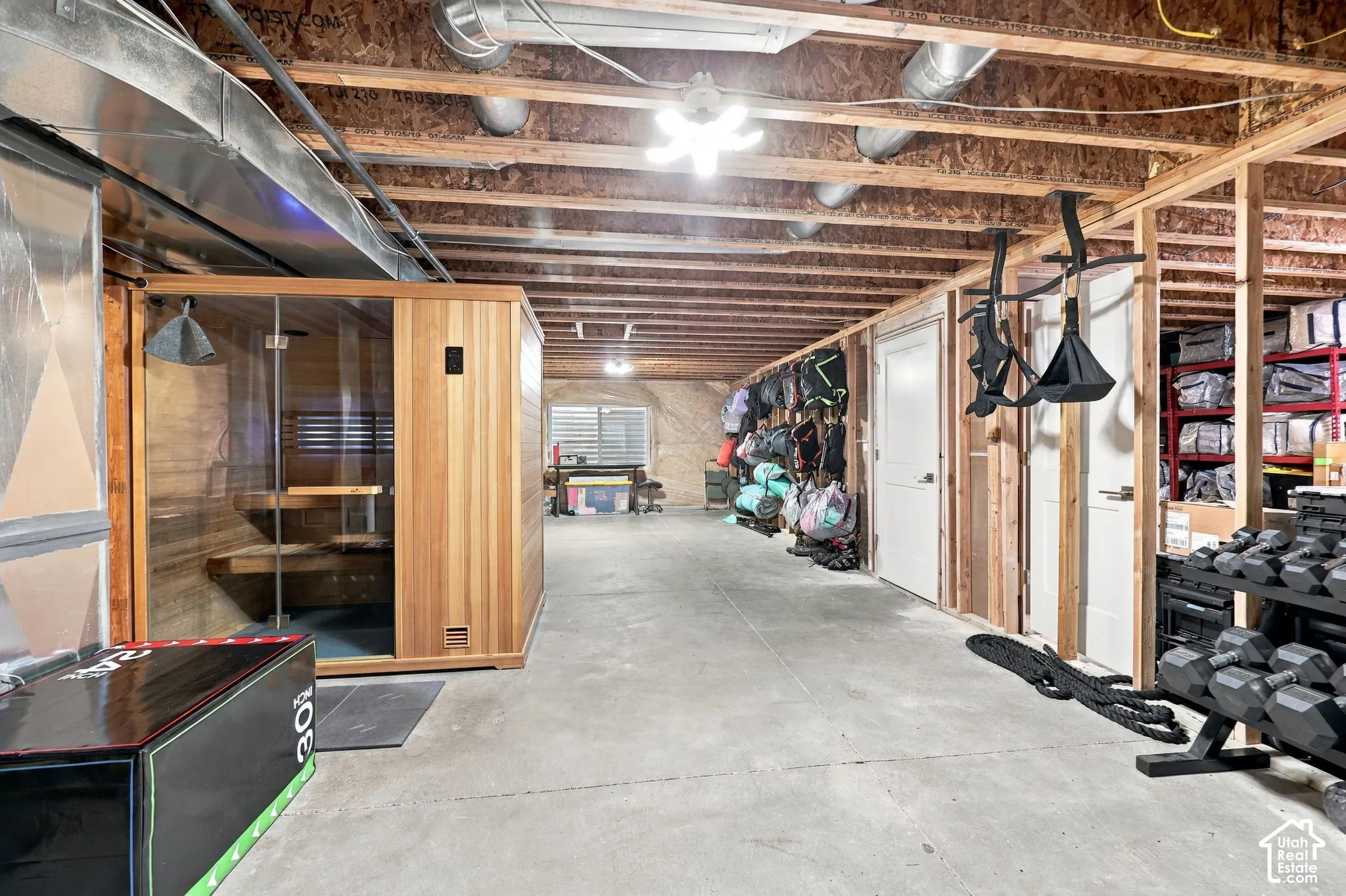 Dedicated fitness area featuring a built-in sauna with a glass door, exposed wood beam ceiling, concrete flooring, and multiple storage doors