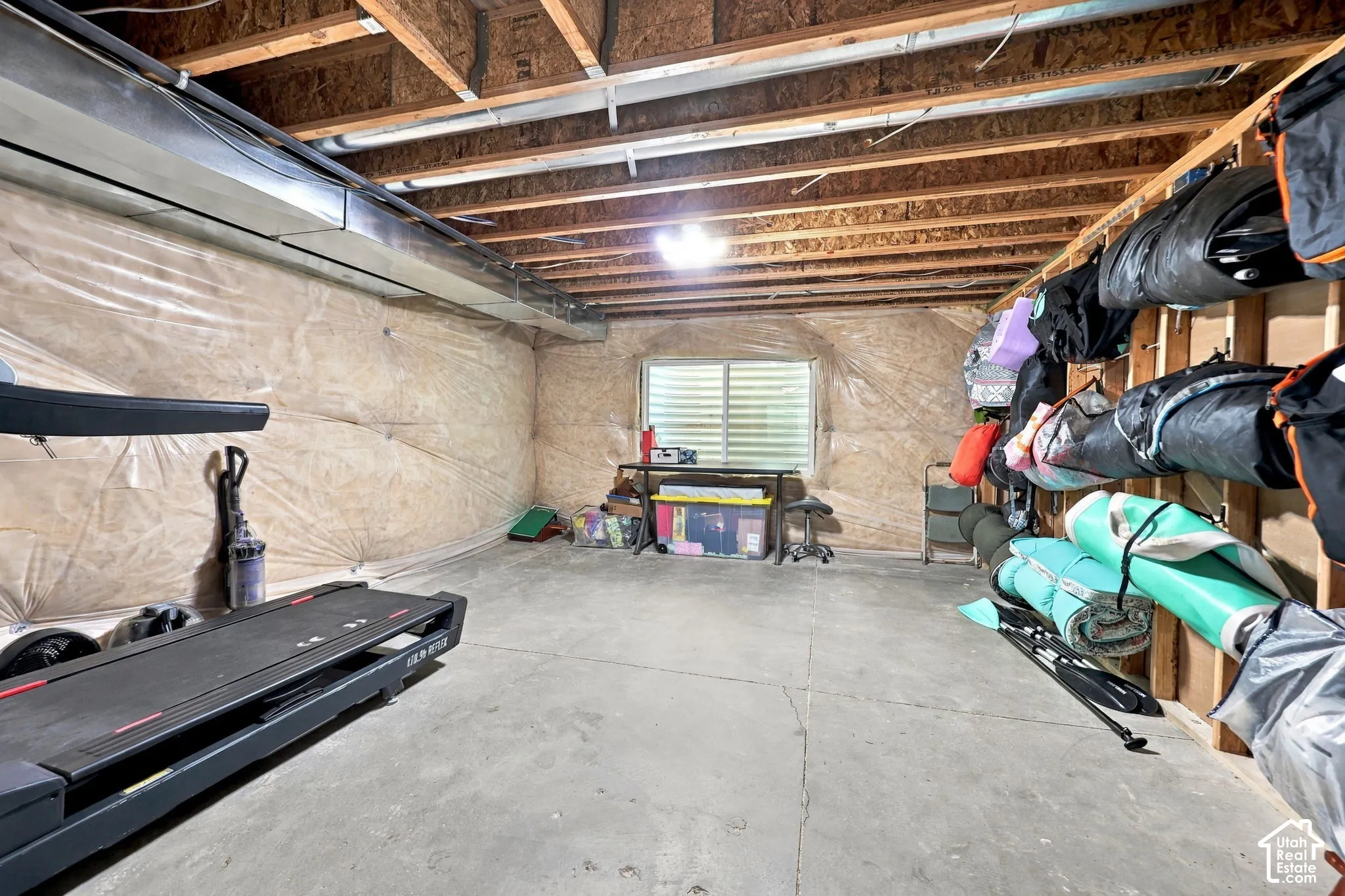 Unfinished basement featuring exposed wood joists, concrete flooring, and a single window with horizontal blinds