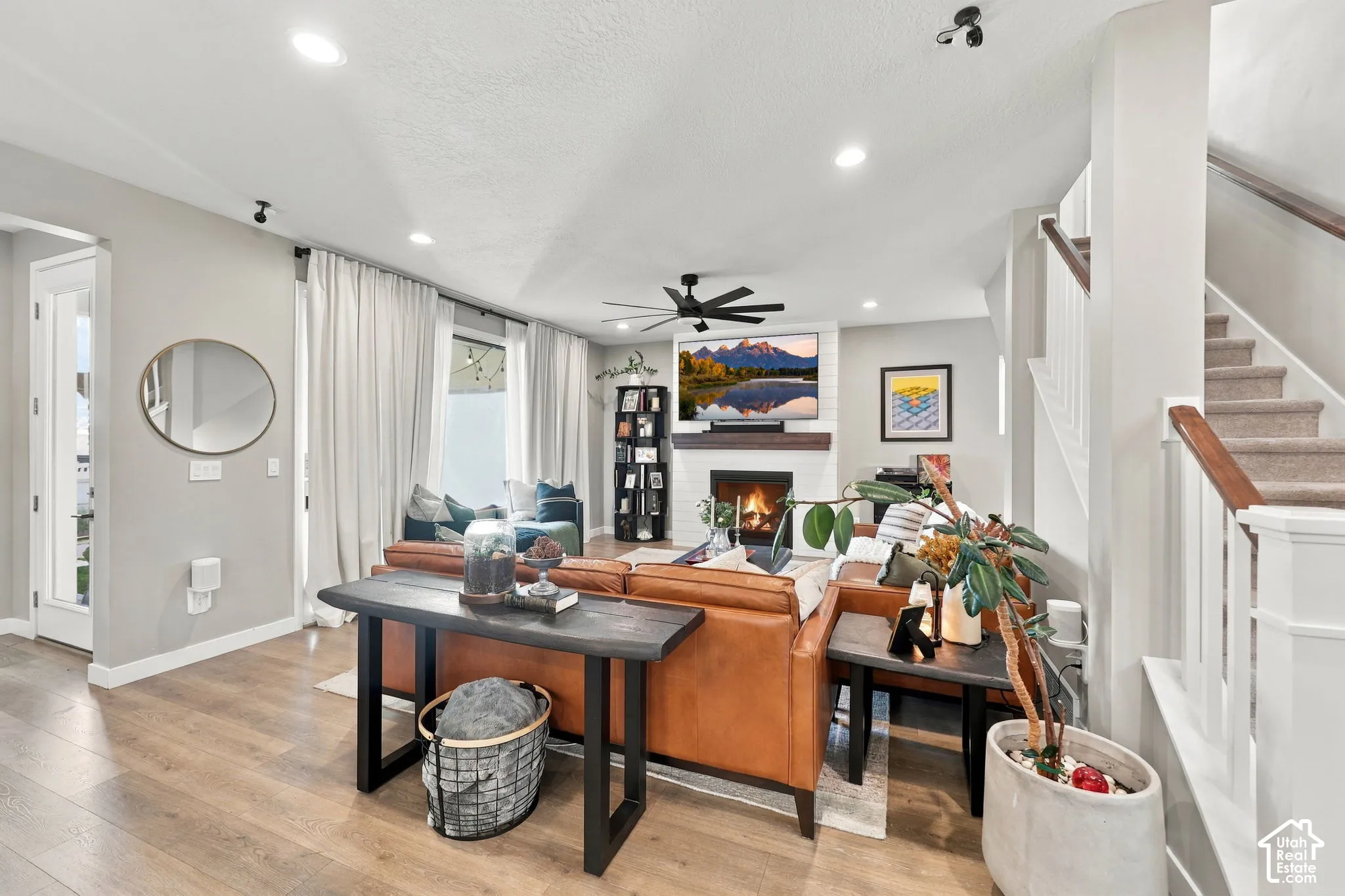 Living area featuring wood-finish flooring, a white tile fireplace with a wood mantle, recessed lighting, and a ceiling fan
