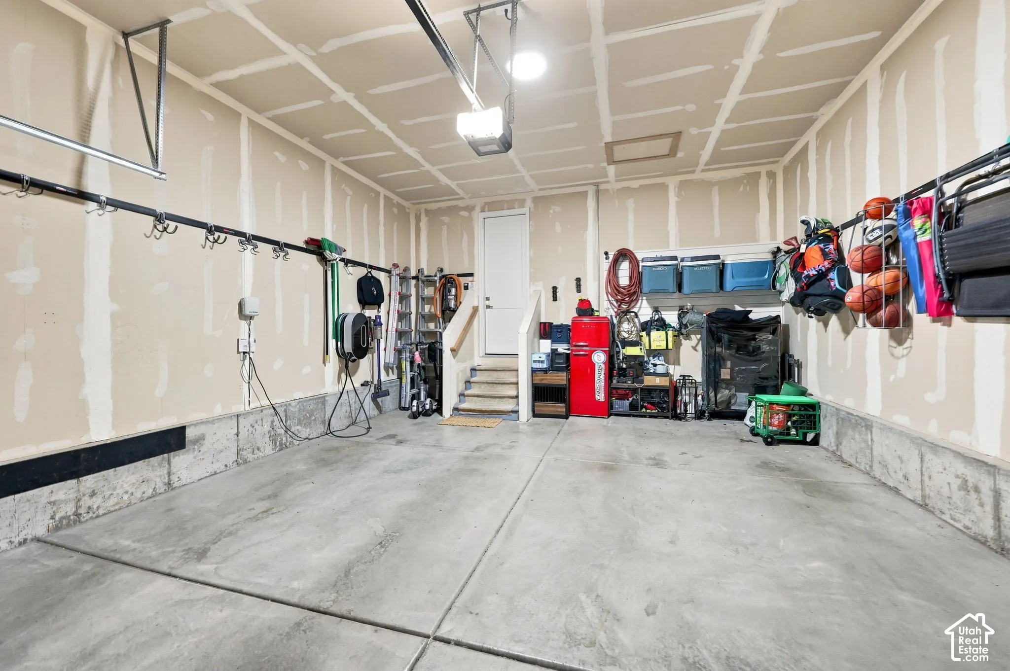 Concrete flooring, unfinished walls, built-in storage hooks, overhead lighting, interior access door