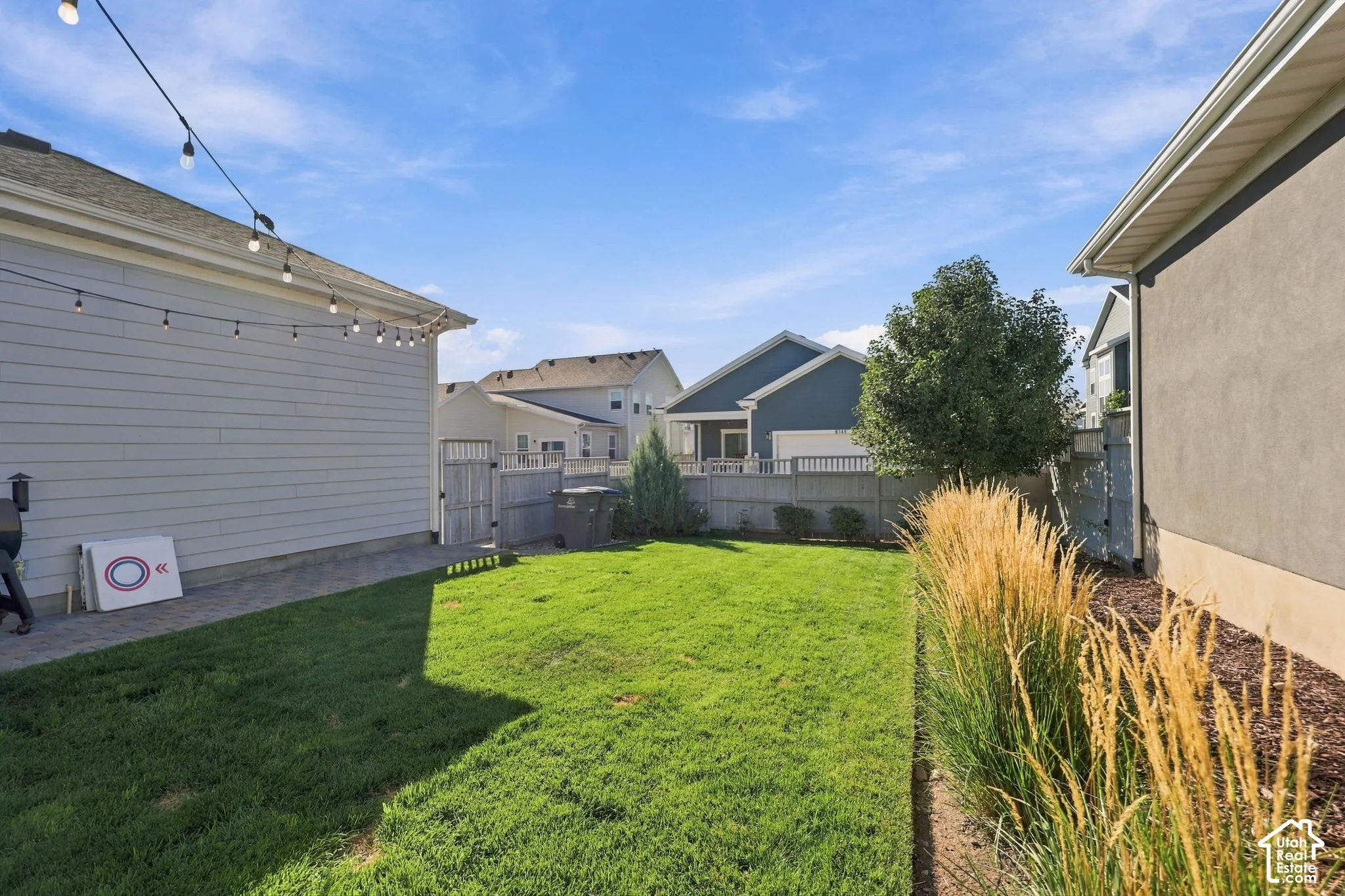 Expansive lawn area with a perimeter fence, mature landscaping, and an exterior string light installation