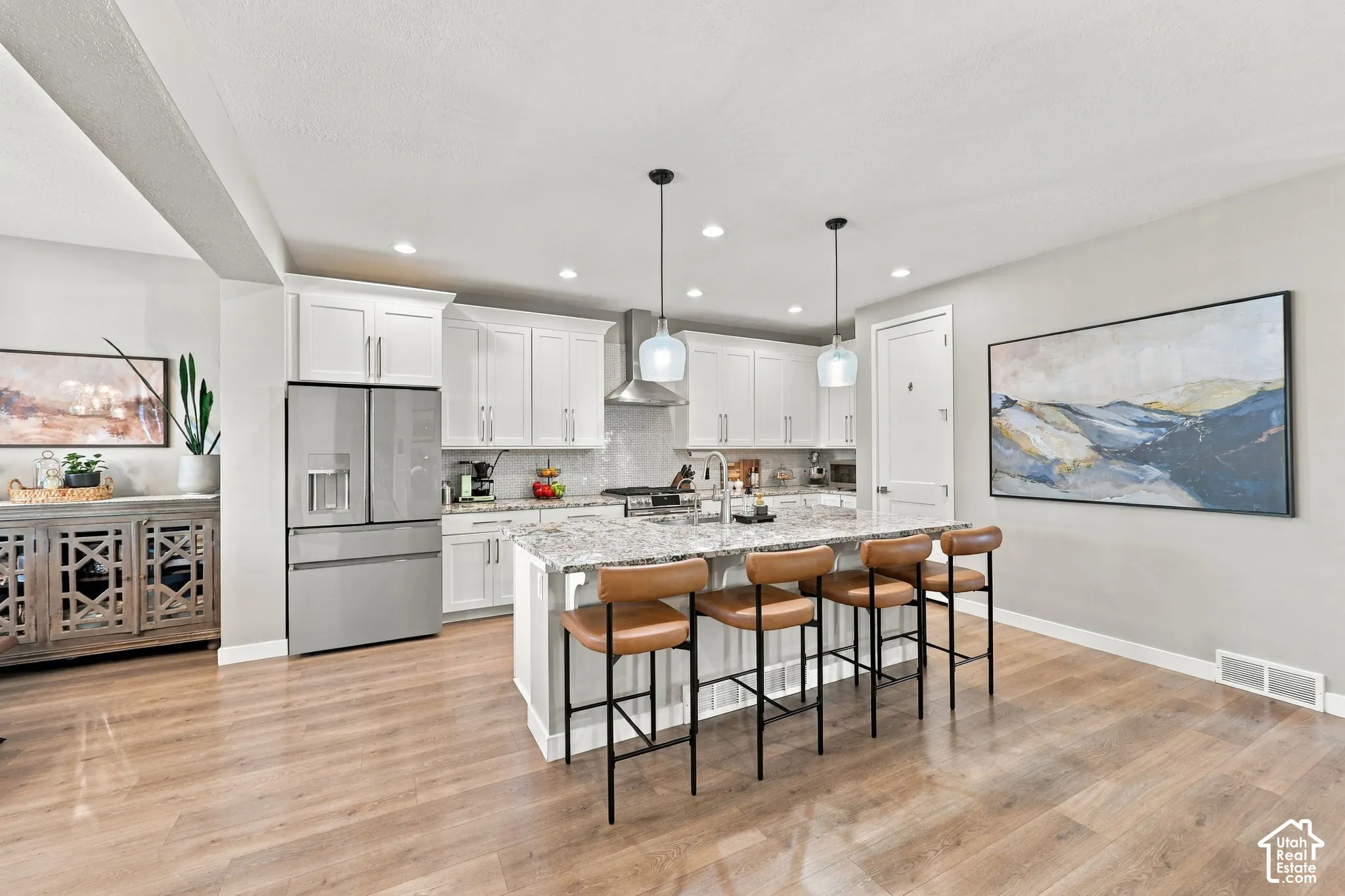 Kitchen featuring white cabinetry, stainless steel appliances, a center island with a stone countertop, pendant lighting, and wood-finish flooring