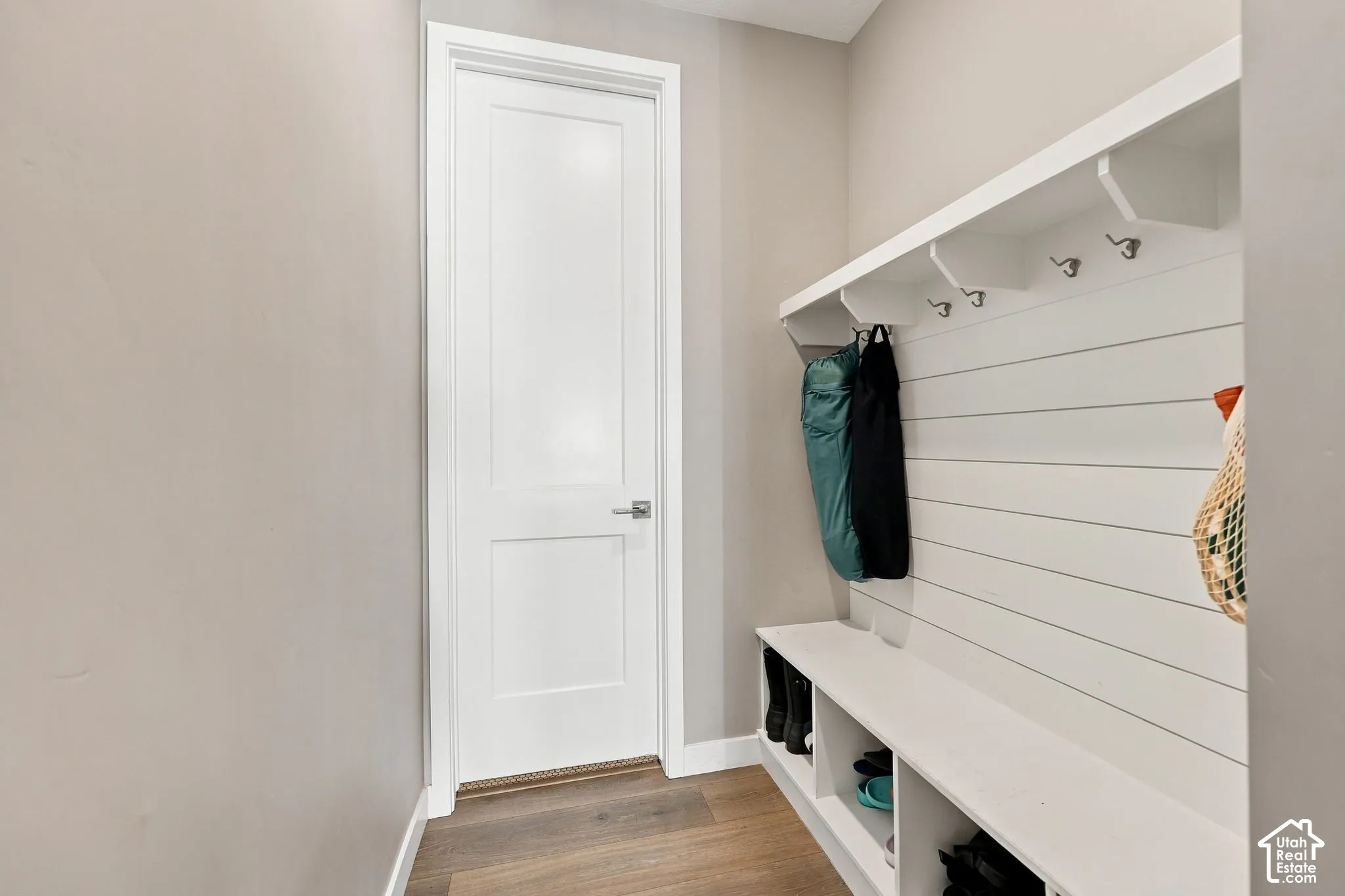 Built-in bench with integrated shelving, wall-mounted coat hooks, white shiplap-style paneling, overhead shelf, and wood-finish flooring