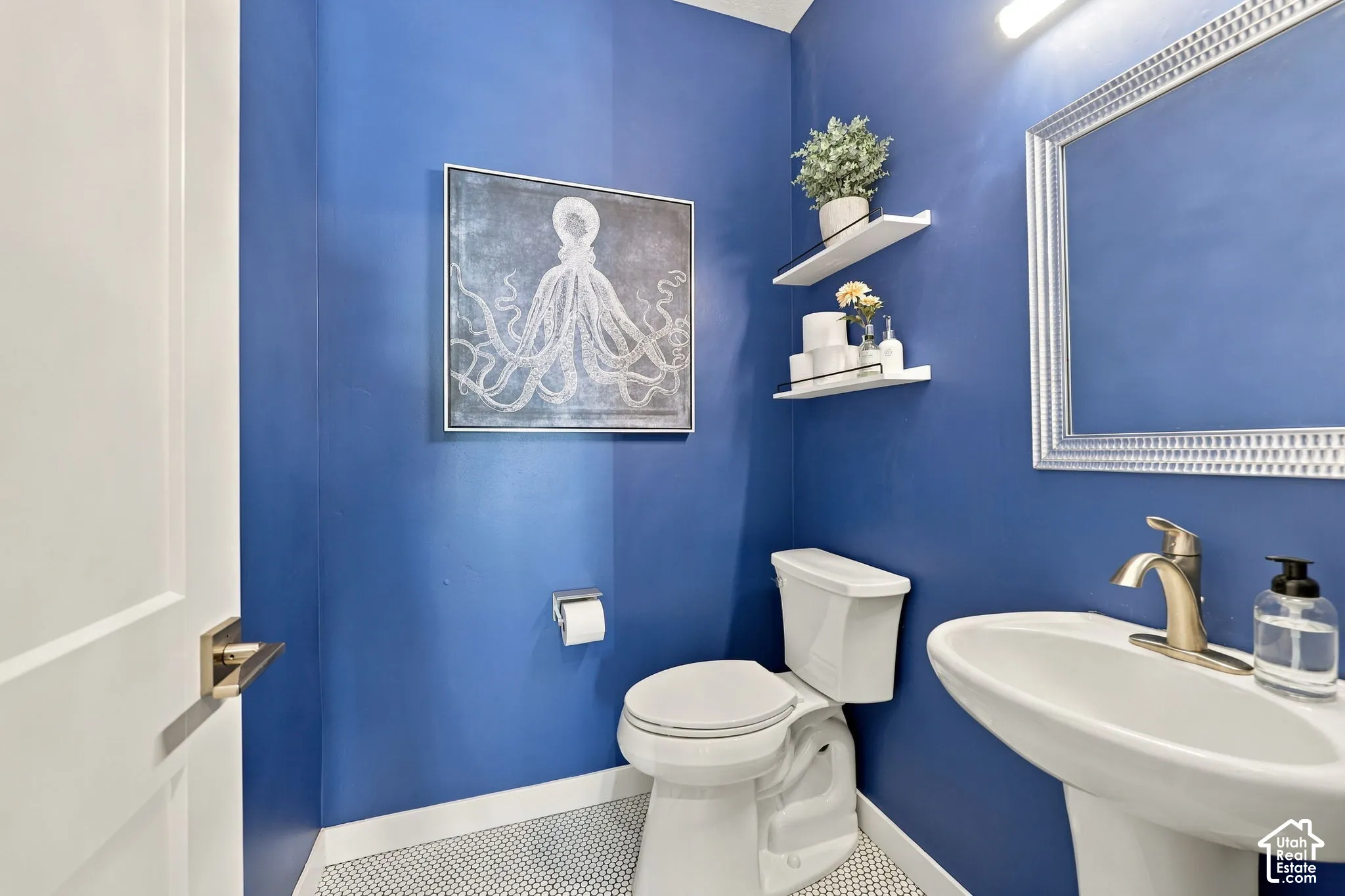 White pedestal sink with a gold-tone faucet, framed mirror, and two white floating shelves