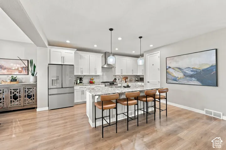 Kitchen featuring white cabinetry, stainless steel appliances, a center island with a stone countertop, pendant lighting, and wood-finish flooring