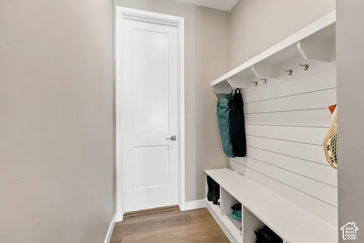 Built-in bench with integrated shelving, wall-mounted coat hooks, white shiplap-style paneling, overhead shelf, and wood-finish flooring