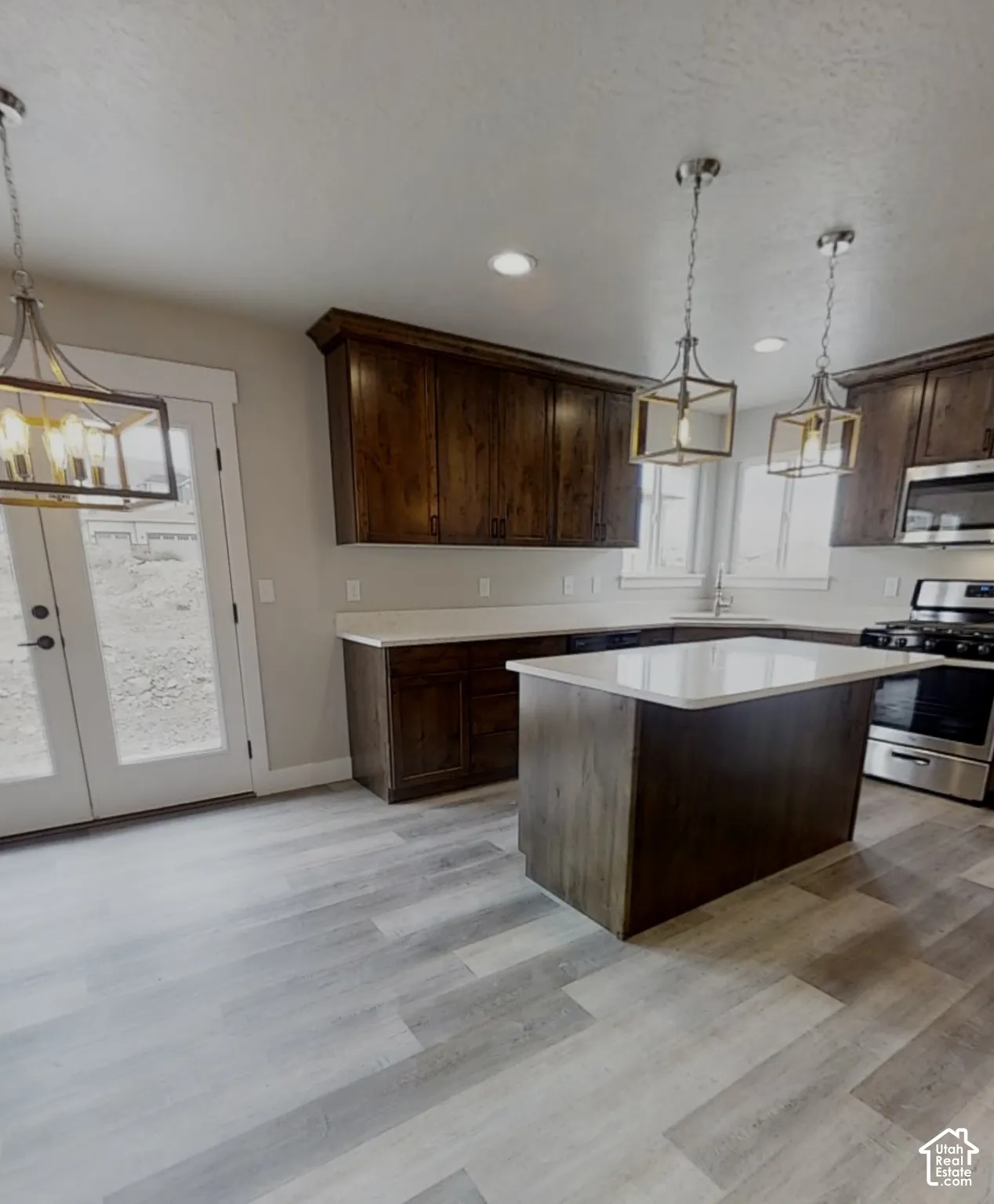 Spacious kitchen featuring wood-finish flooring, dark wood cabinetry, light-toned countertops, a kitchen island, and stainless steel appliances