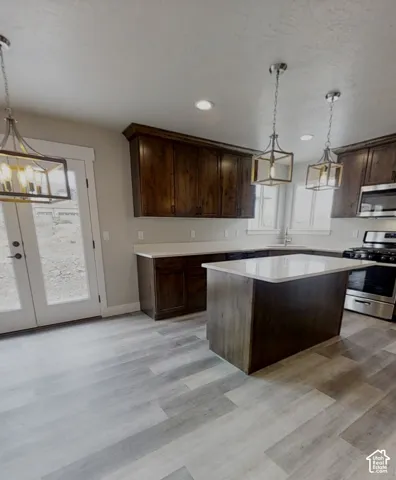 Spacious kitchen featuring wood-finish flooring, dark wood cabinetry, light-toned countertops, a kitchen island, and stainless steel appliances