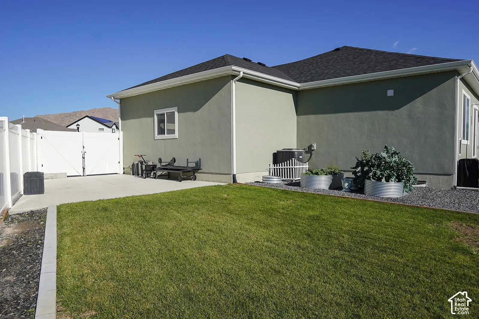 Expansive backyard featuring a manicured lawn, concrete patio, white vinyl fencing, and raised garden beds