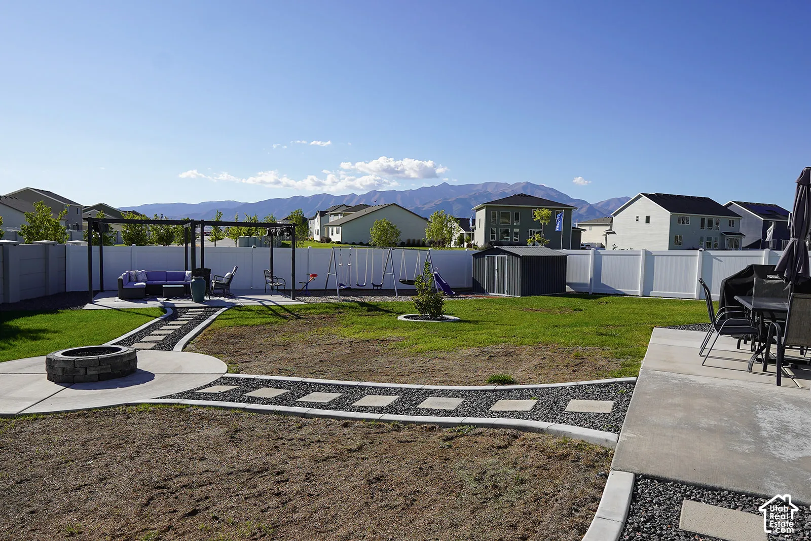 Expansive backyard featuring a stone fire pit, concrete patio, pergola, and white privacy fencing