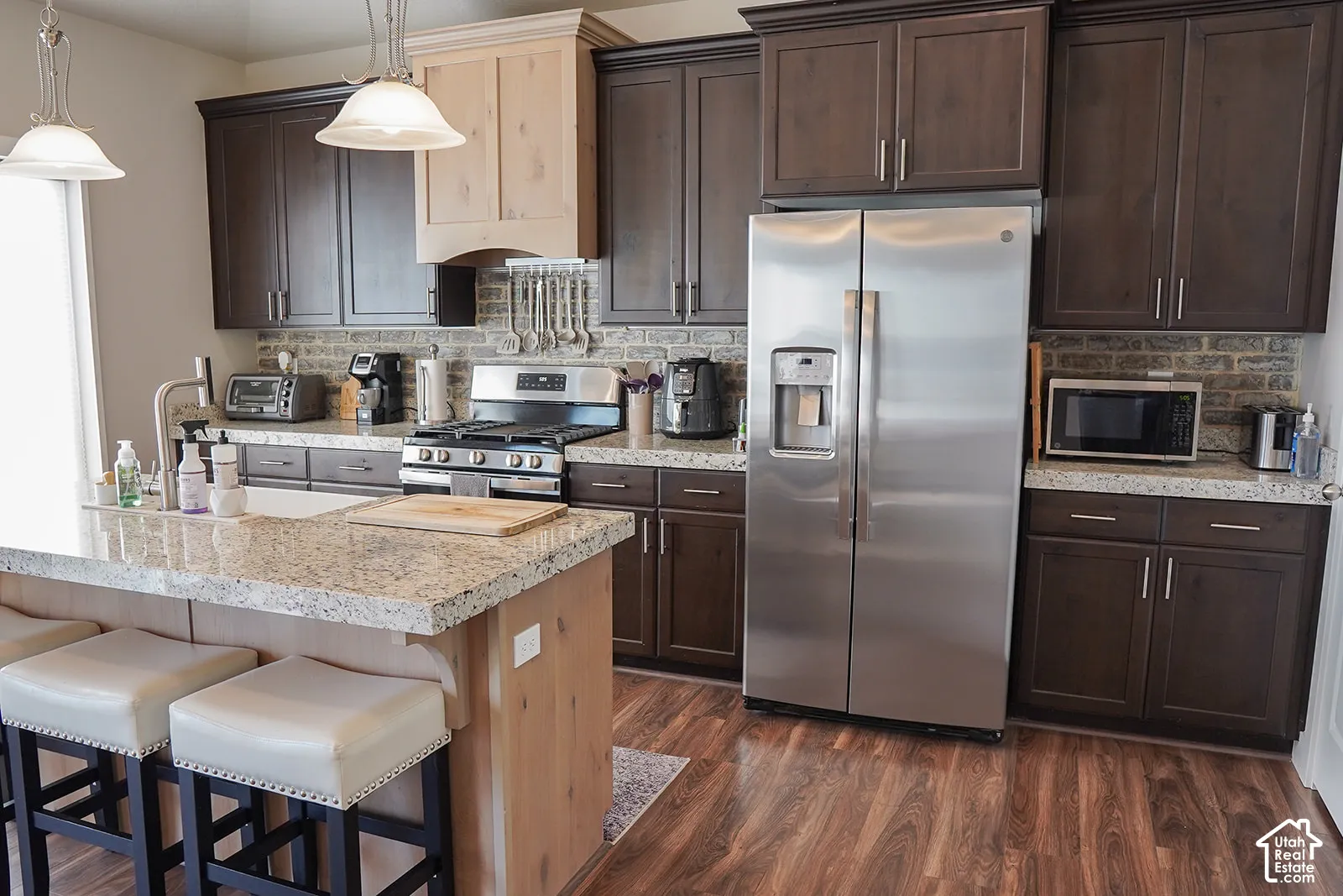 Kitchen featuring a granite-finish island, wood-finish flooring, two-tone cabinetry, a stainless steel refrigerator, and a gas range