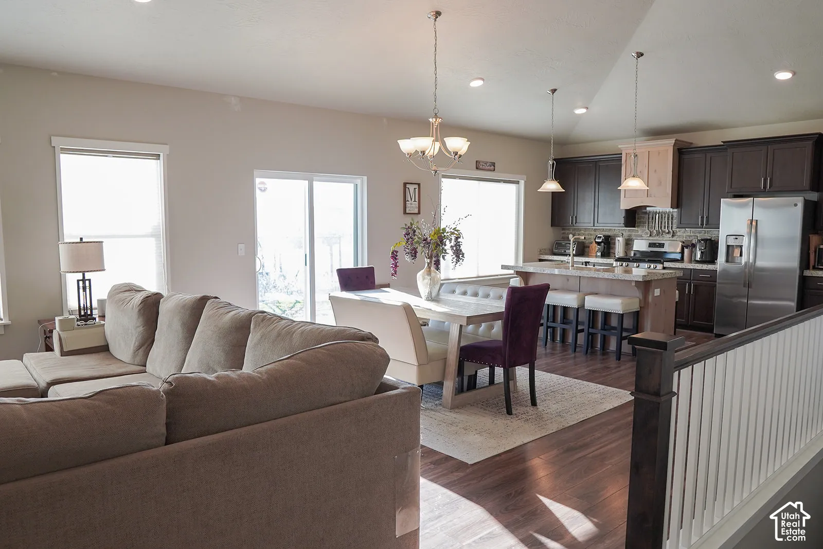 Open-concept living area with wood-finish flooring, a kitchen island with seating, dark wood cabinetry, stainless steel appliances, and recessed lighting