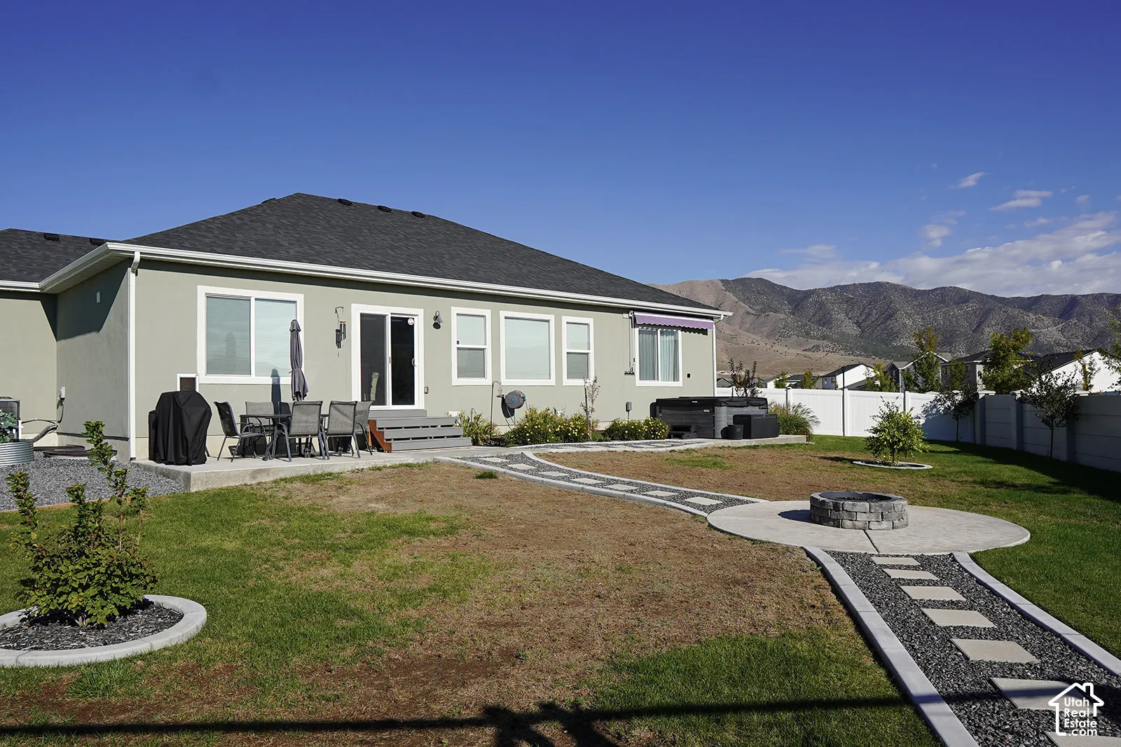 Spacious backyard with a concrete patio, gravel and paver pathways, built-in fire pit, and a hot tub