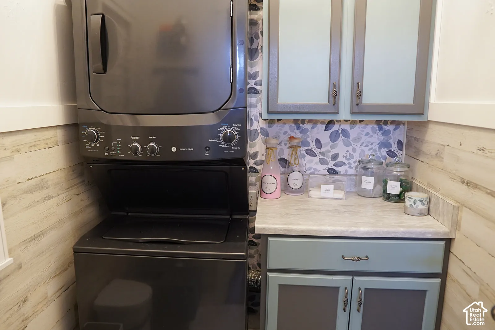 Stackable washer and dryer, patterned backsplash, wood-finish wall panels, and light-toned countertops