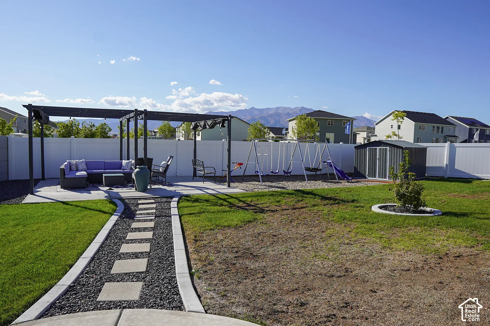 Backyard featuring a concrete patio with pergola, white vinyl fencing, a metal storage shed, and a stone-lined pathway