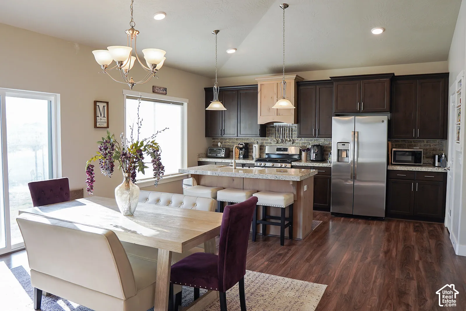 Spacious dining area with a glass sliding door, wood-finish flooring, and a kitchen featuring dark wood cabinetry, stainless steel appliances, and a central island with bar seating