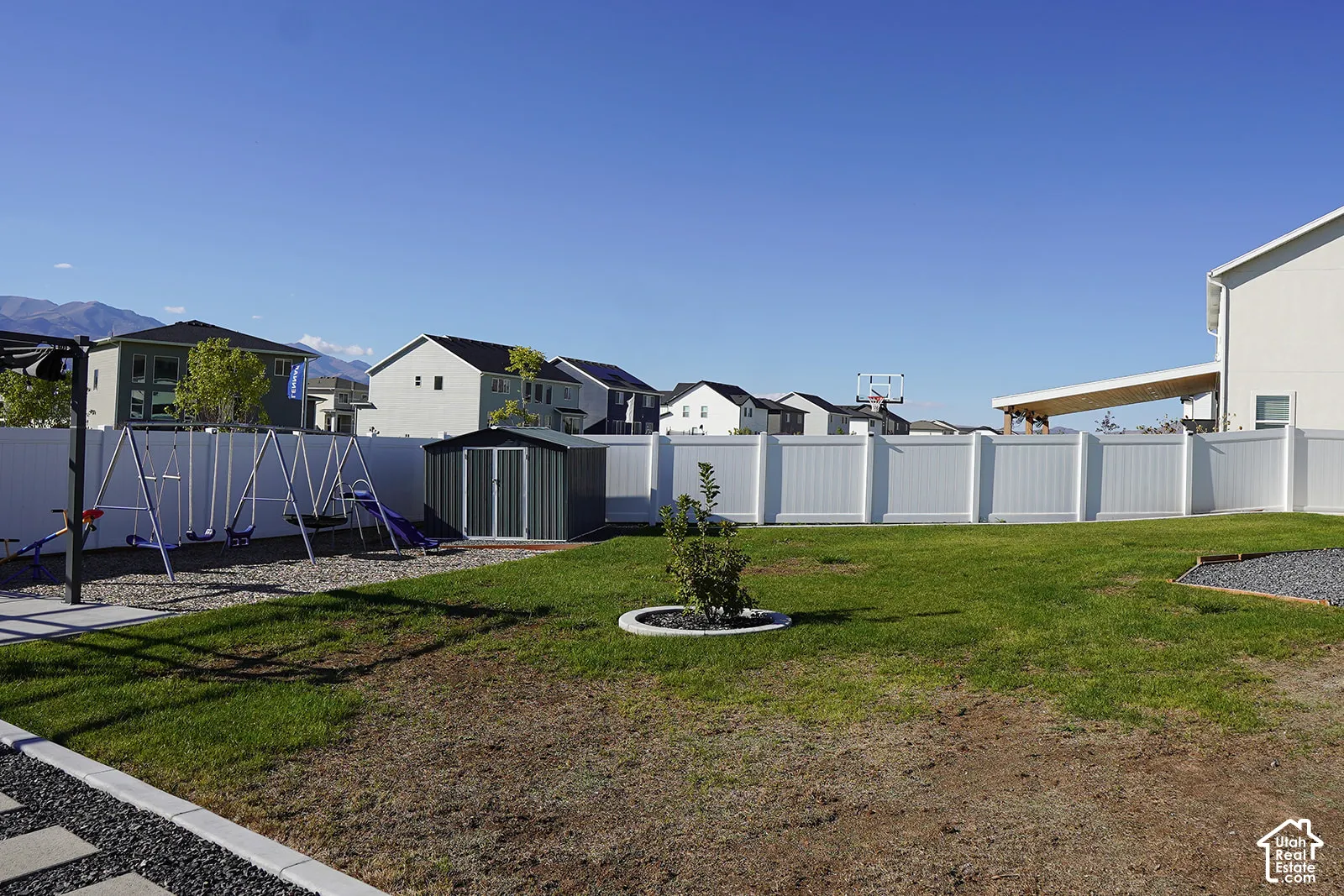 Expansive backyard featuring a manicured lawn, white privacy fencing, and a dedicated play area
