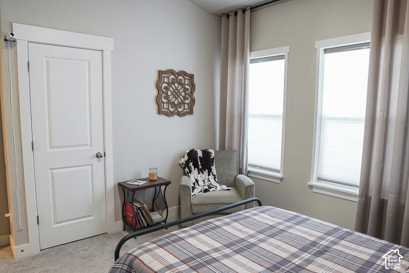 Plush carpet flooring, white painted interior door, two windows with blinds, and light-colored wall paint