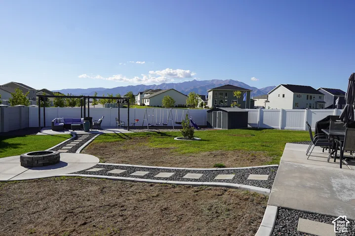 Expansive backyard featuring a stone fire pit, concrete patio, pergola, and white privacy fencing